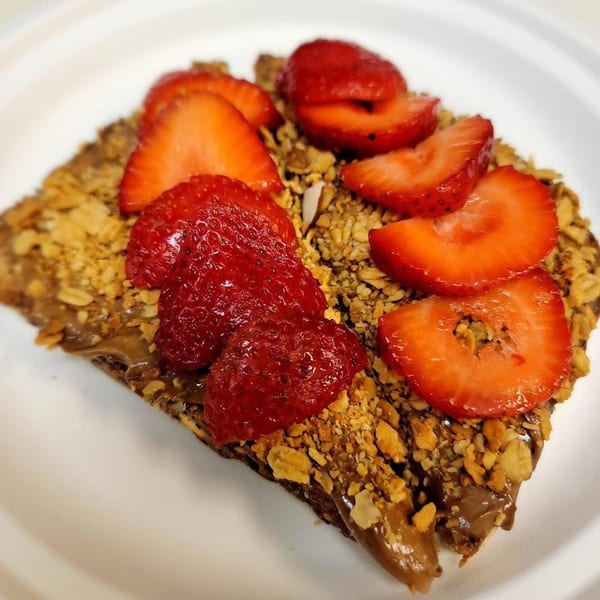 A Grouchy John's Coffee crepe with chocolate, granola, and fresh strawberries on a white plate.