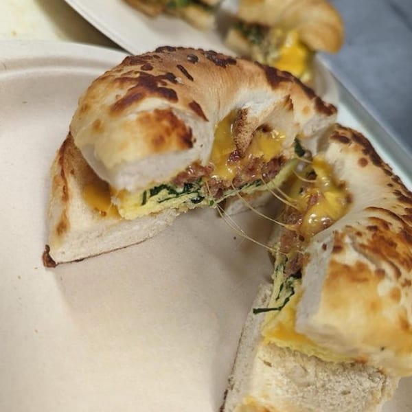 A cheesy bagel sandwich with egg, bacon, and spinach, pulled apart with melted cheese strings.
