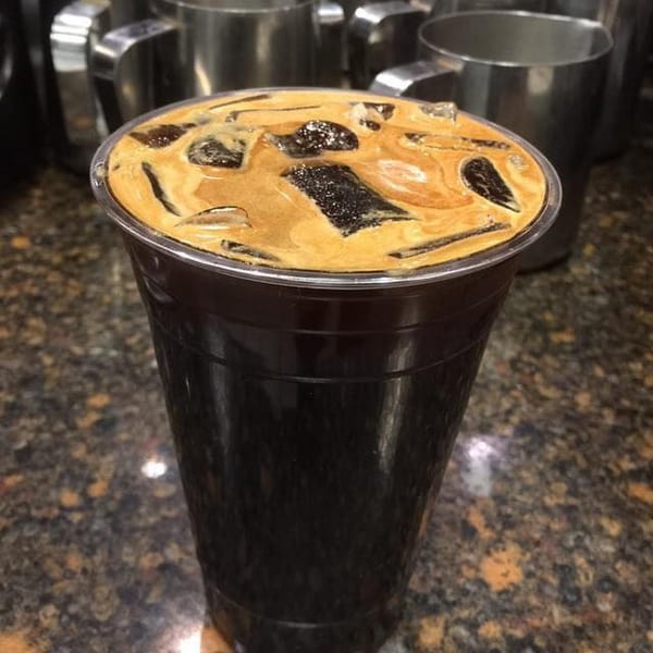 A close-up of a Grouchy John's Coffee iced coffee with ice cubes and a creamy top layer.
