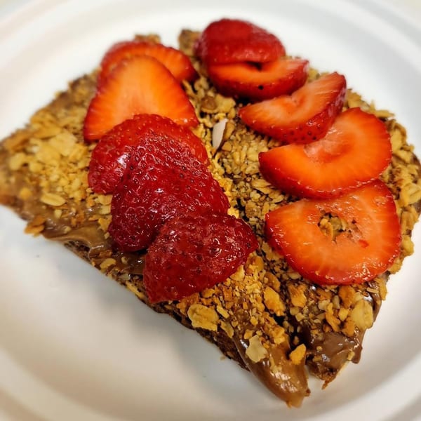 A Grouchy John's Coffee crepe topped with chocolate spread, granola, and fresh strawberries.
